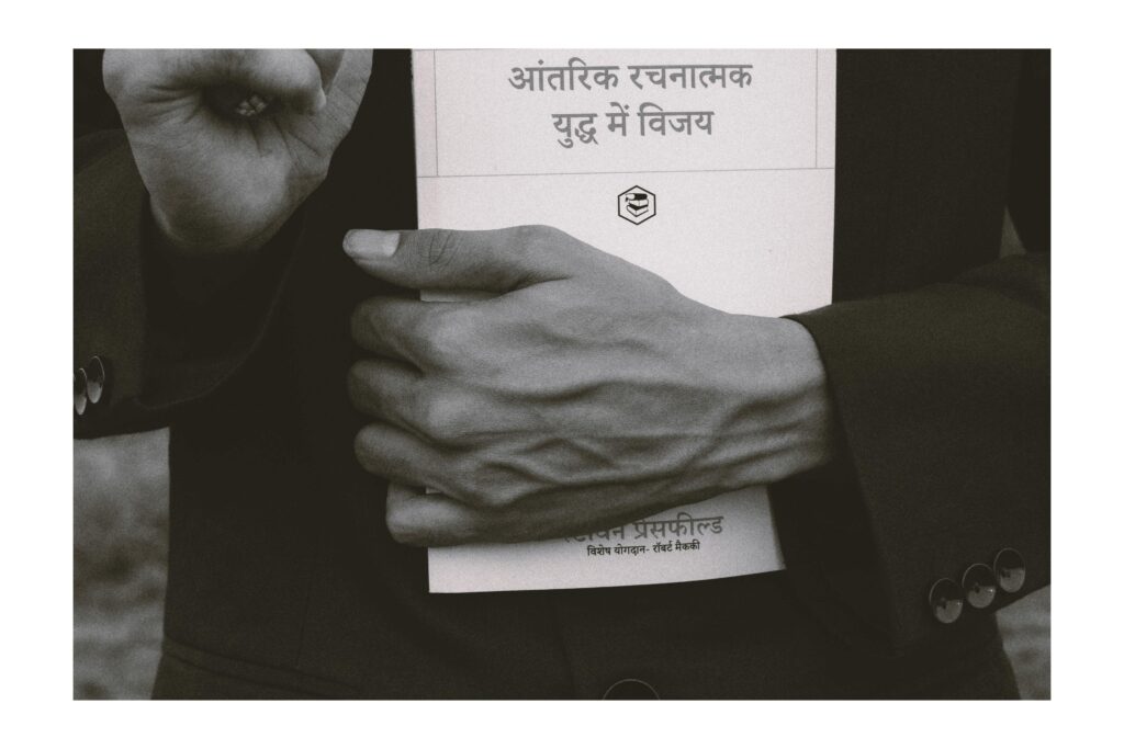 Hand of a person holding a hindi language book.